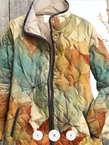 A colorful, quilted jacket featuring an artistic leaf design in shades of blue, orange, and cream, hanging on a wooden background.