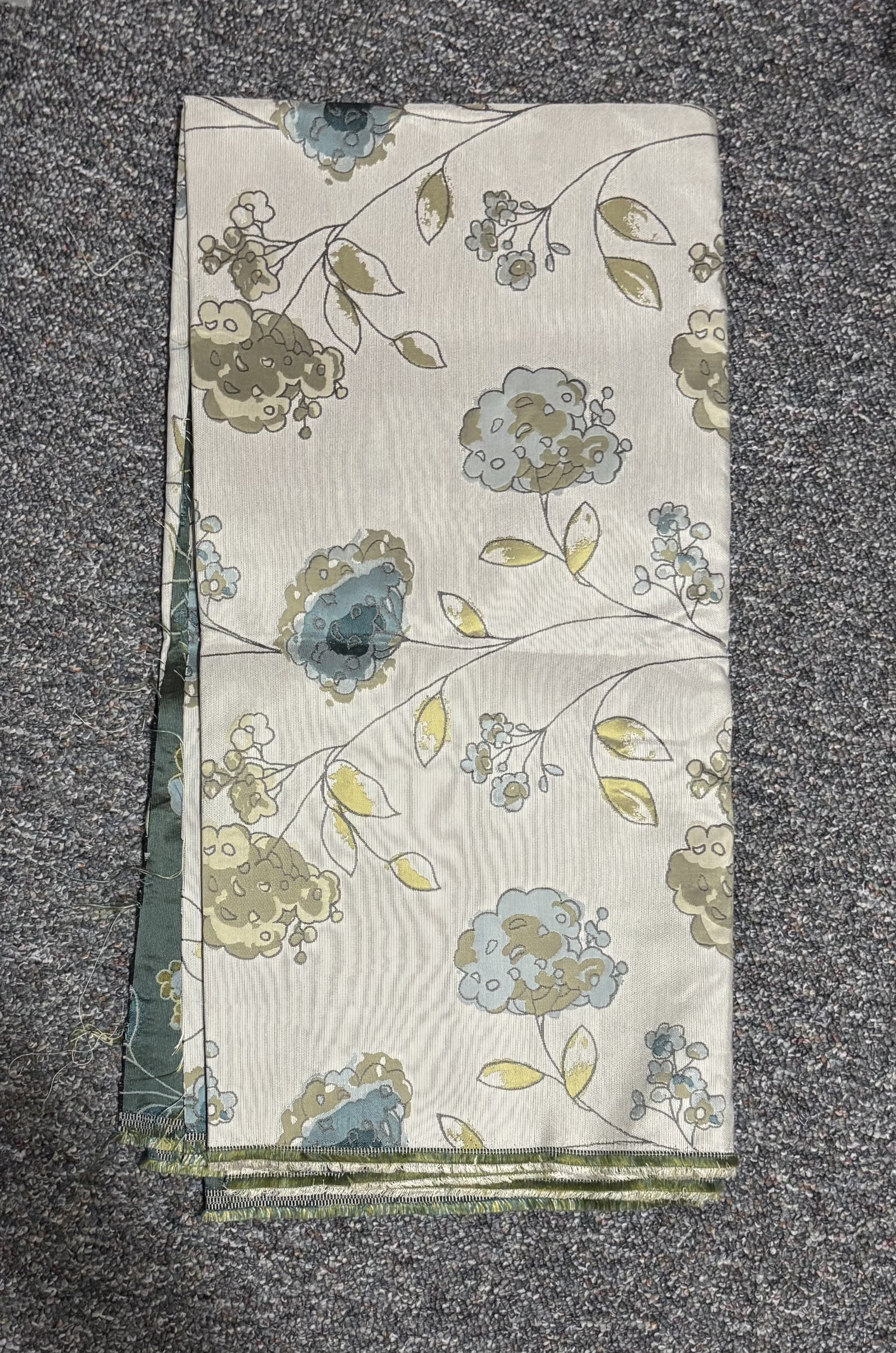A folded piece of fabric featuring a floral pattern in shades of blue, green, and beige, set against a light background.